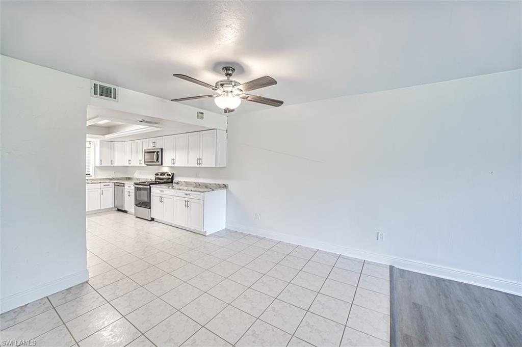 Kitchen with stainless steel appliances, white cabinets, a ceiling fan, light stone countertops, and a tray ceiling