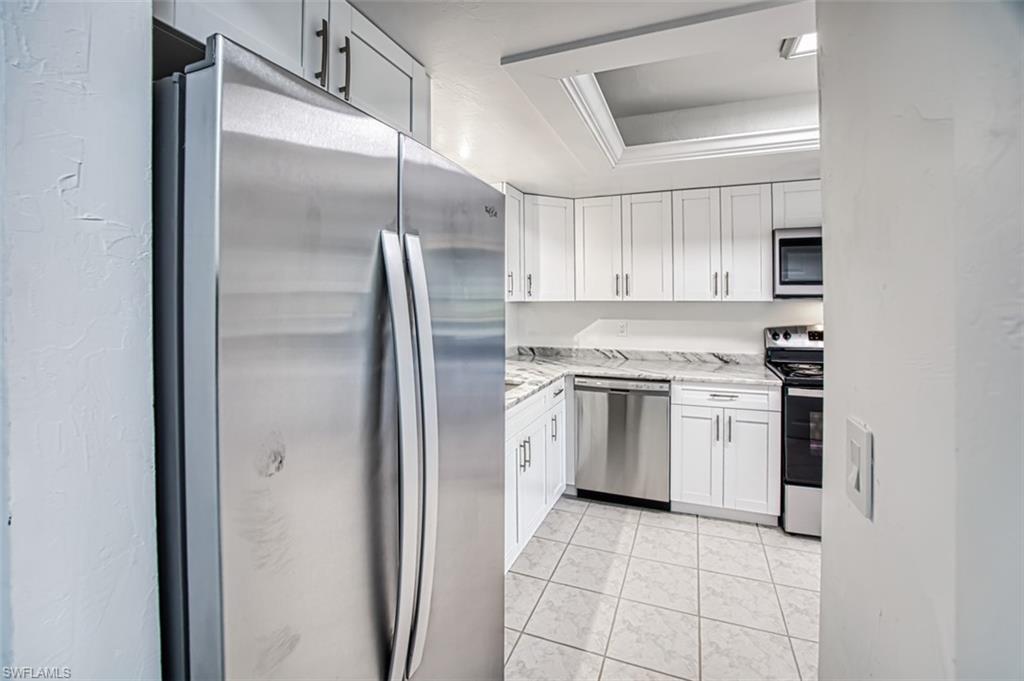 Kitchen with stainless steel appliances, white cabinetry, a tray ceiling, and light tile patterned floors
