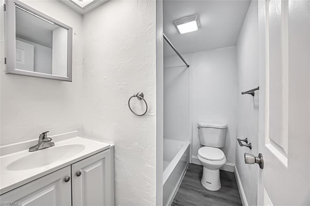 Full bathroom with a textured wall,  shower combination, dark wood-style flooring, and vanity