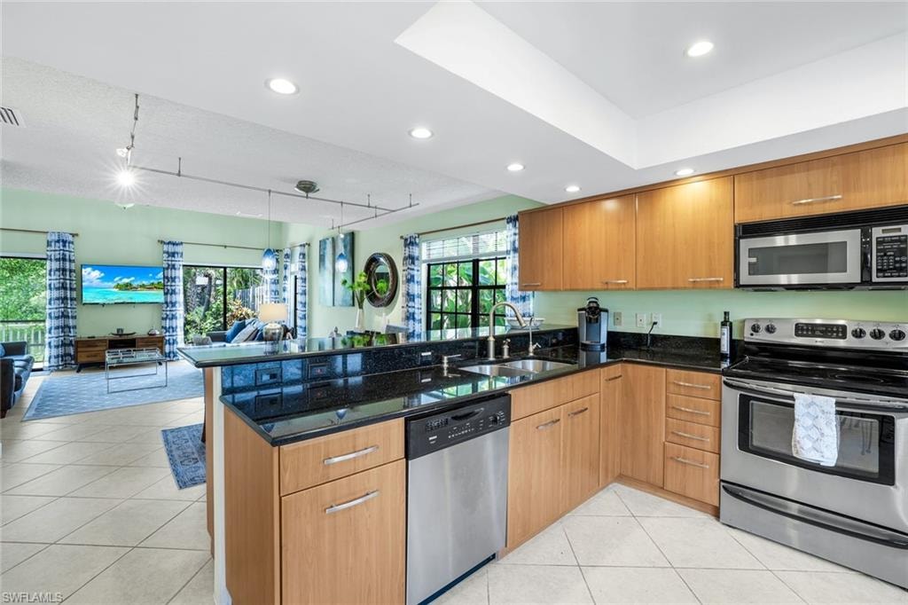 Kitchen featuring stainless steel appliances, open floor plan, brown cabinets, dark stone counters, and recessed lighting