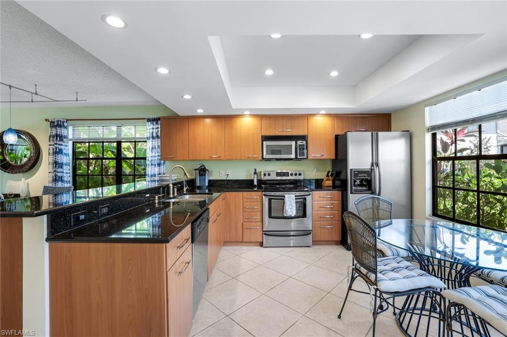 Kitchen with stainless steel appliances, dark stone counters, light tile patterned floors, recessed lighting, and a peninsula