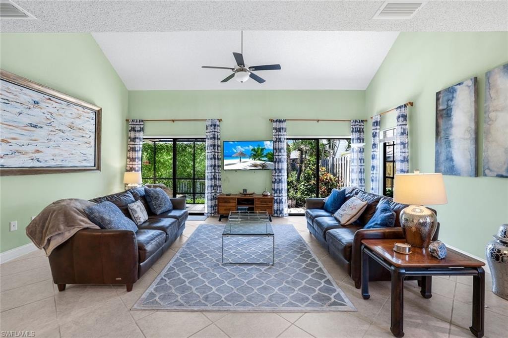 Living area featuring lofted ceiling, tile patterned flooring, a textured ceiling, and a ceiling fan