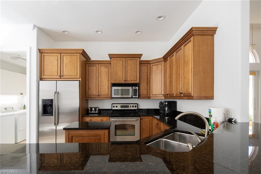 Kitchen with brown cabinetry, stainless steel appliances, dark stone countertops, washing machine and dryer, and recessed lighting
