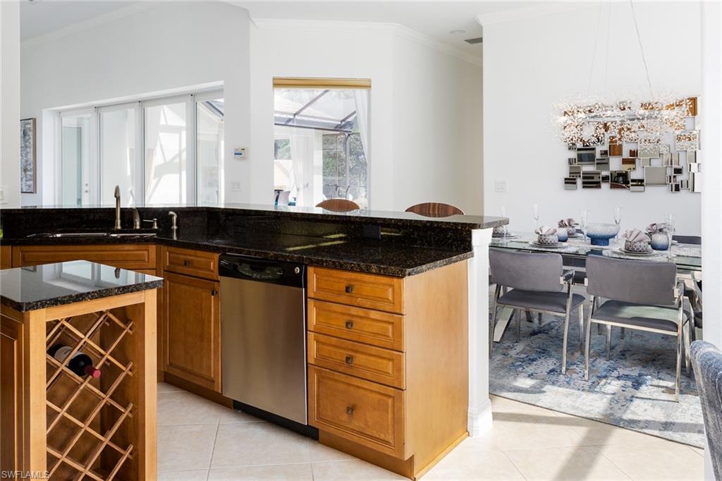 Kitchen with ornamental molding, dark stone counters, brown cabinetry, light tile patterned floors, and stainless steel dishwasher