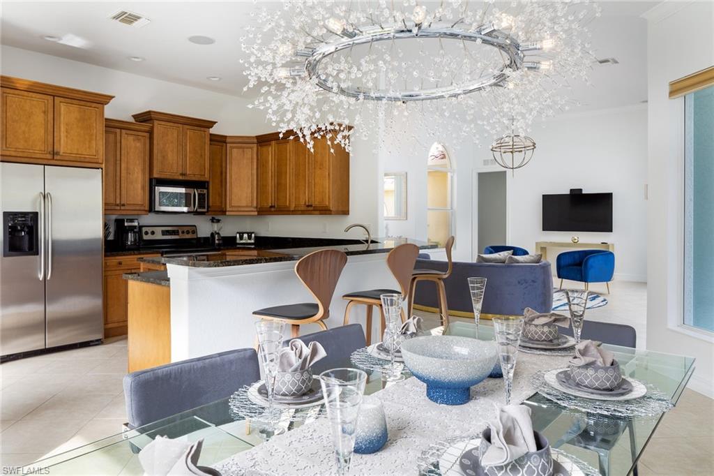Kitchen featuring brown cabinets, stainless steel appliances, dark stone countertops, light tile patterned floors, and a kitchen breakfast bar