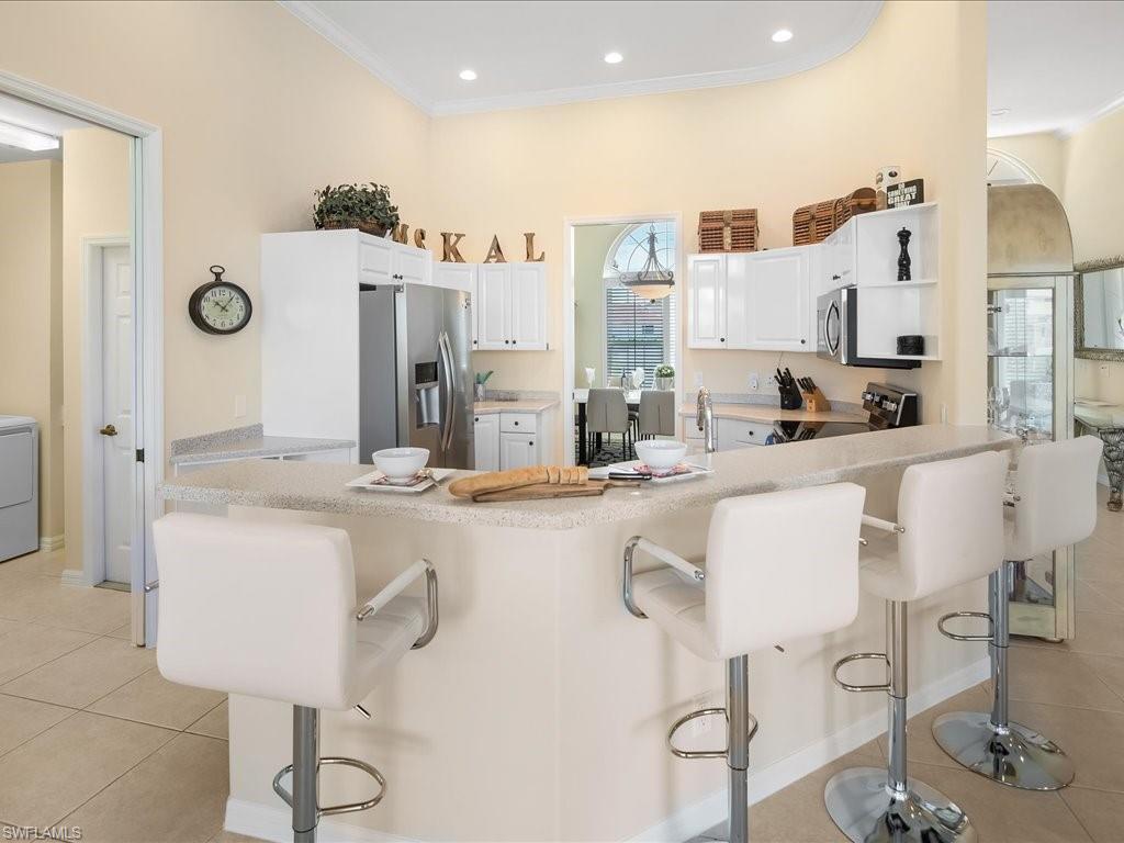Kitchen featuring a breakfast bar area, light tile patterned floors, appliances with stainless steel finishes, white cabinets, and crown molding
