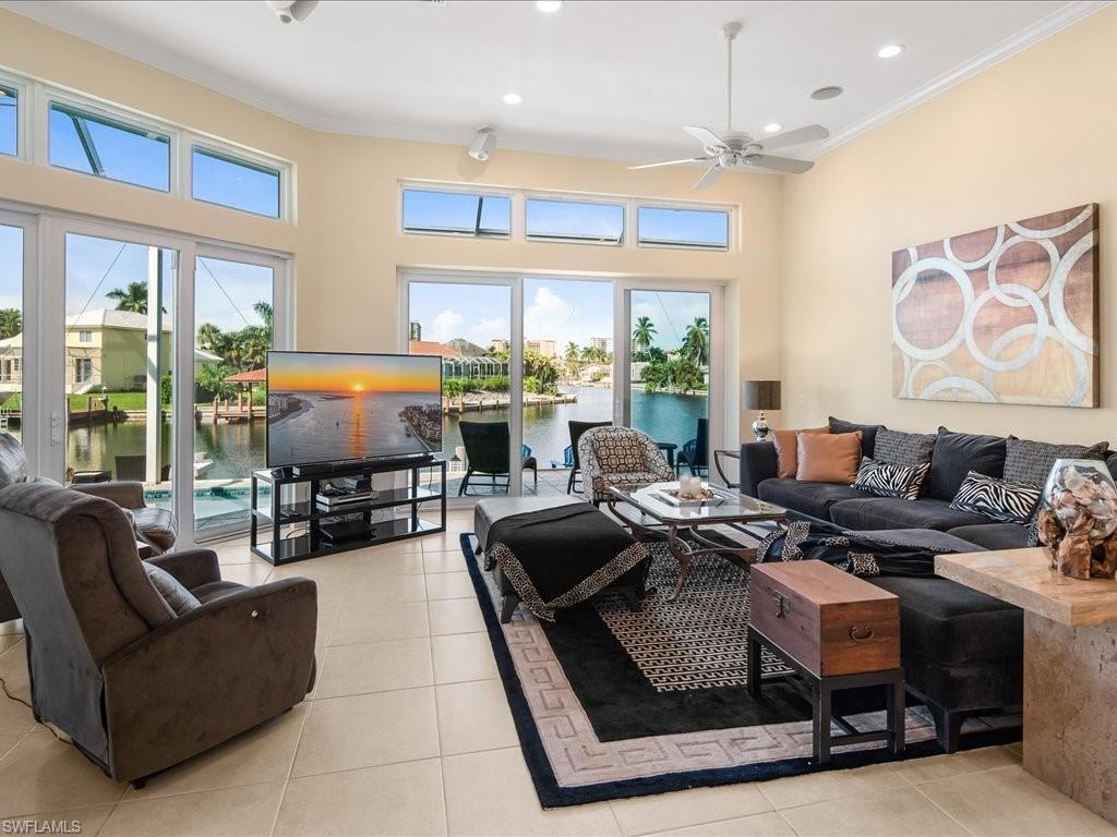 Living area with light tile patterned flooring, recessed lighting, crown molding, ceiling fan, and a towering ceiling