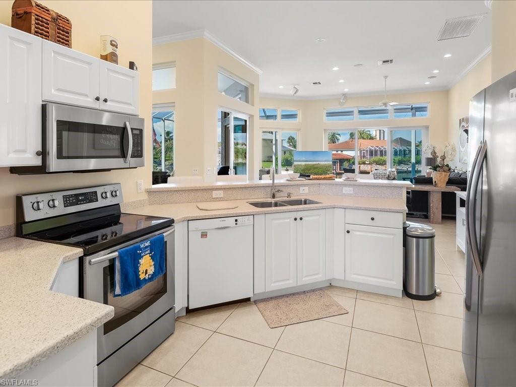 Kitchen with appliances with stainless steel finishes, light tile patterned flooring, white cabinetry, crown molding, and recessed lighting