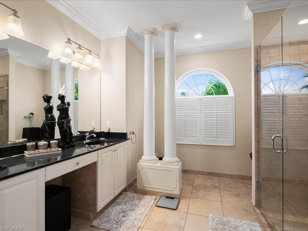 Full bath with ornamental molding, double vanity, a shower stall, and light tile patterned floors