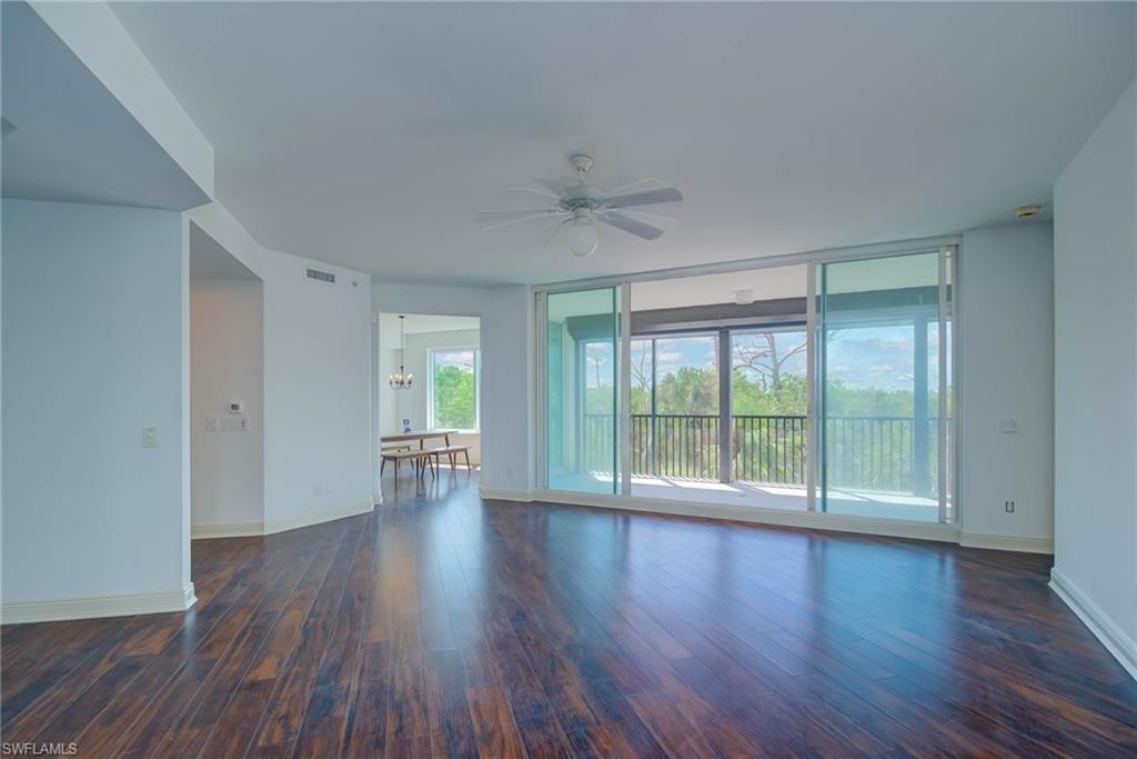 Unfurnished living room with dark wood-style flooring, floor to ceiling windows, ceiling fan, and a chandelier
