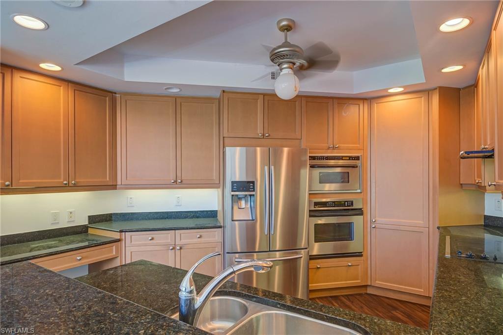 Kitchen featuring recessed lighting, appliances with stainless steel finishes, a tray ceiling, and dark stone counters