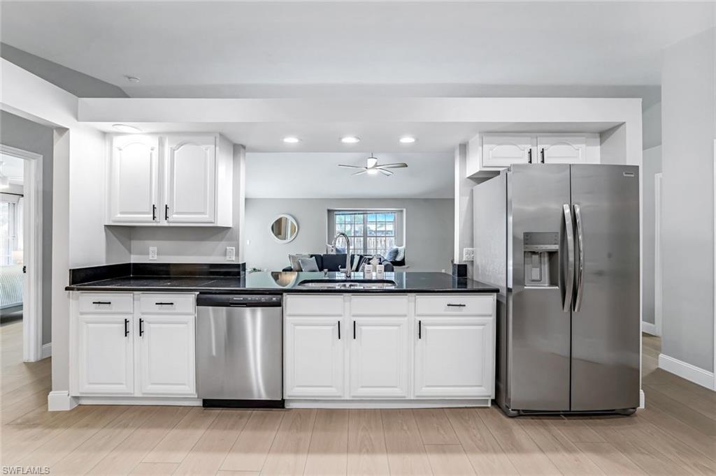 Kitchen with stainless steel appliances, white cabinets, recessed lighting, light wood-style floors, and dark stone countertops