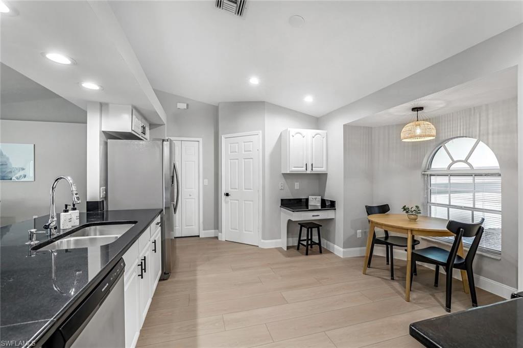 Kitchen featuring dark stone counters, light wood-type flooring, decorative light fixtures, appliances with stainless steel finishes, and white cabinets