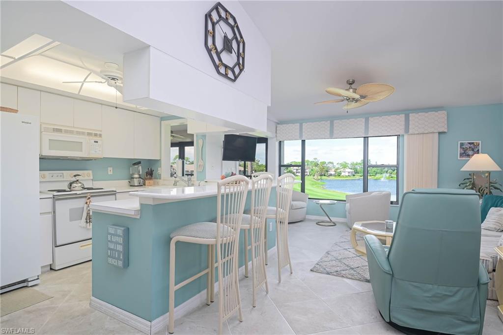 Kitchen featuring white appliances, light countertops, open floor plan, a ceiling fan, and a breakfast bar