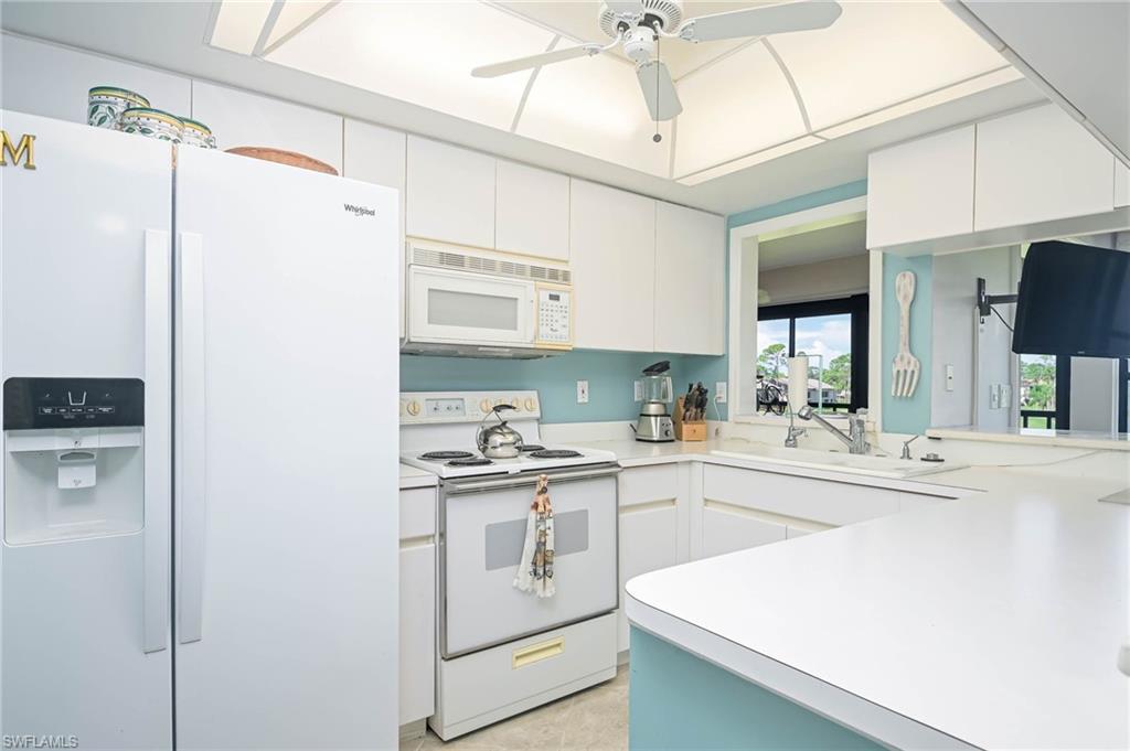 Kitchen with white appliances, light countertops, white cabinetry, and a ceiling fan