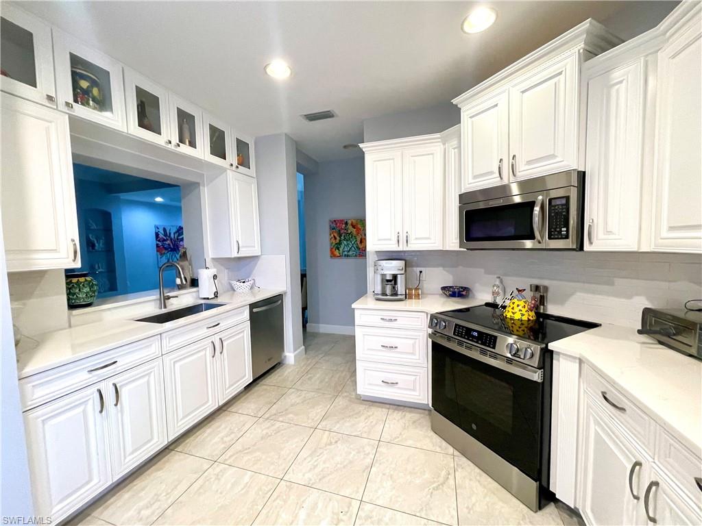 Kitchen featuring appliances with stainless steel finishes, white cabinets, glass insert cabinets, and recessed lighting