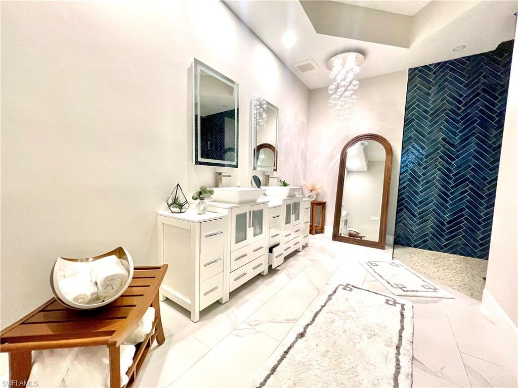 Full bath featuring double vanity, light marble finish flooring, and a chandelier