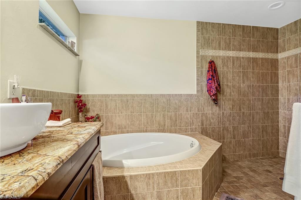 Bathroom with double vanity, a bath, light tile patterned flooring, tile walls, and recessed lighting