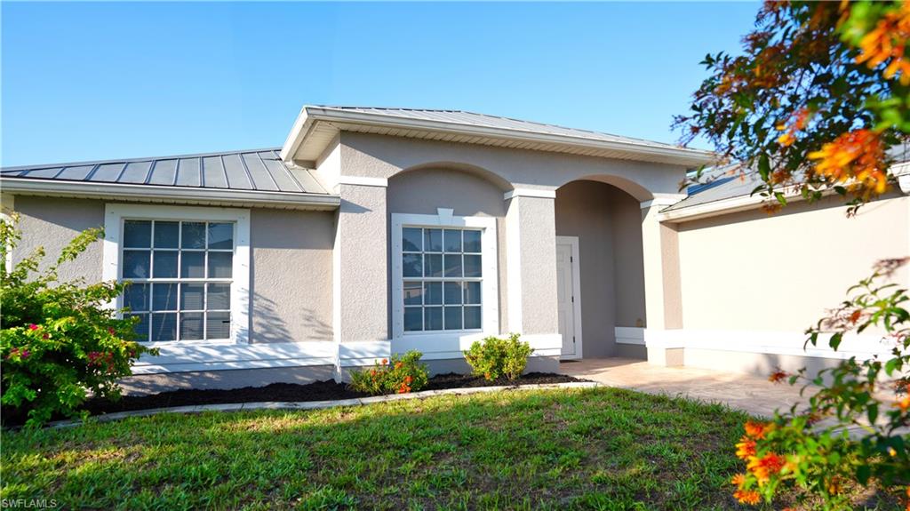 Doorway to property with a metal roof, a standing seam roof, stucco siding, and a yard