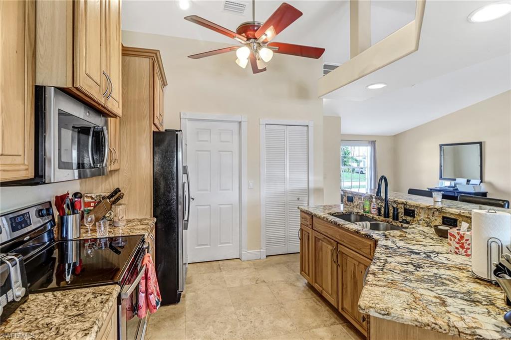 Kitchen featuring stainless steel appliances, lofted ceiling, light stone counters, a breakfast bar, and a kitchen island with sink