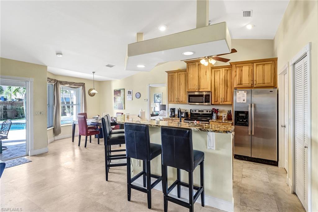 Kitchen featuring appliances with stainless steel finishes, recessed lighting, light stone counters, ceiling fan, and lofted ceiling