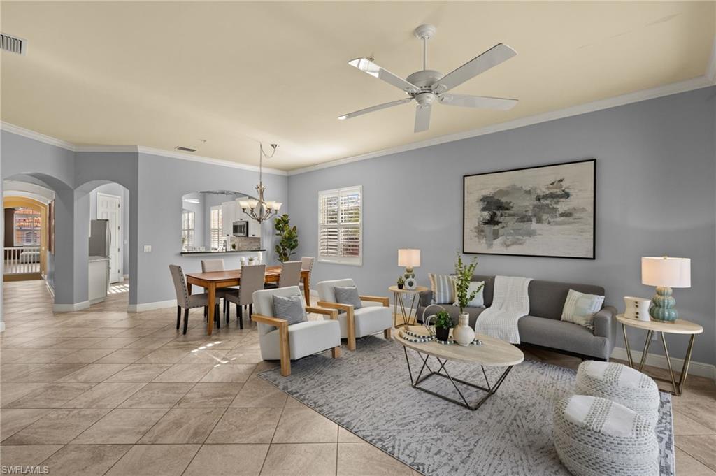 Living area featuring arched walkways, crown molding, and ceiling fan with notable chandelier