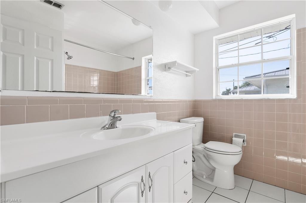 Bathroom with tile walls, tile patterned flooring, a wealth of natural light, and toilet