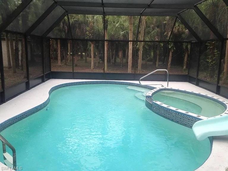 View of swimming pool with a sunroom, a water slide, a lanai, and a pool with connected hot tub