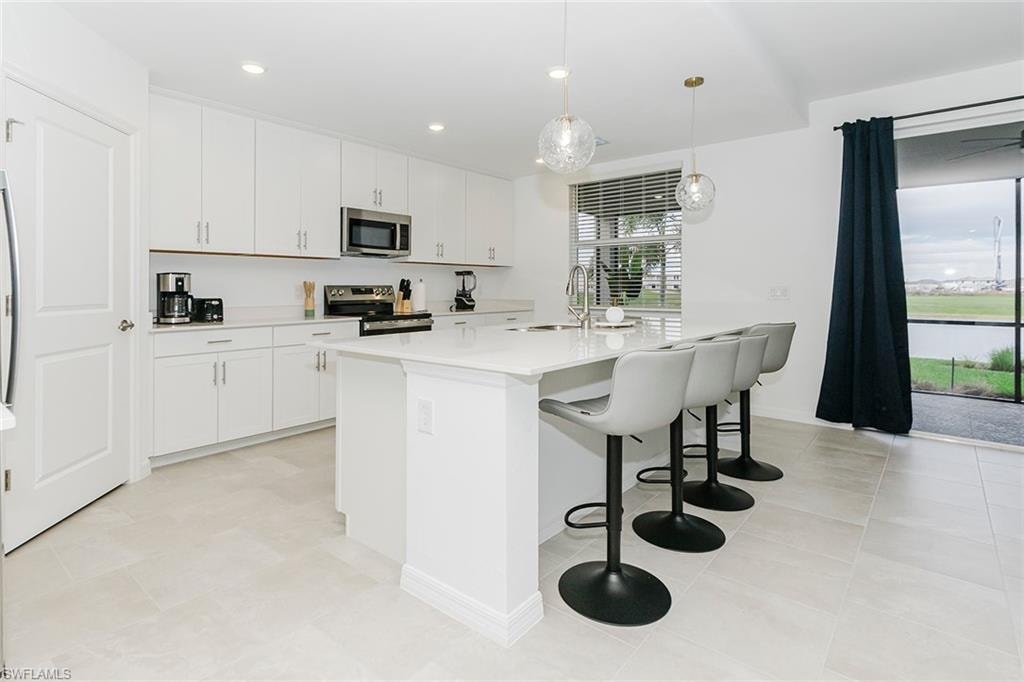 Kitchen with stainless steel appliances, pendant lighting, white cabinets, a center island with sink, and a breakfast bar area
