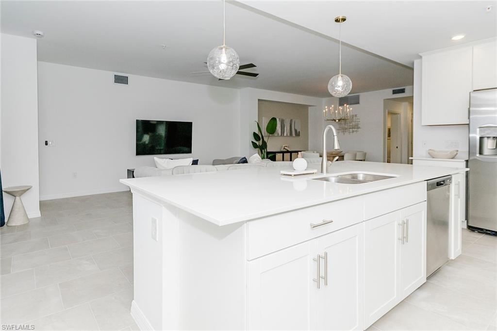 Kitchen with white cabinets, stainless steel appliances, a ceiling fan, open floor plan, and a kitchen island with sink