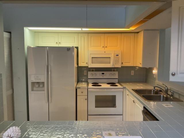 Kitchen with tile counters, white appliances, tasteful backsplash, and white cabinetry