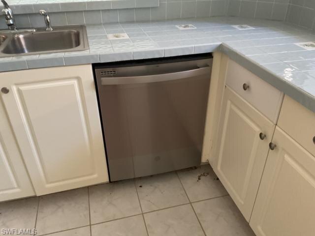 Kitchen view of stainless steel dishwasher, white cabinetry, tile countertops, and tasteful backsplash
