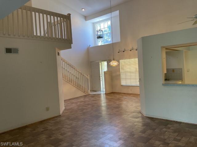 Unfurnished living room with a towering ceiling, stairway, and ceiling fan