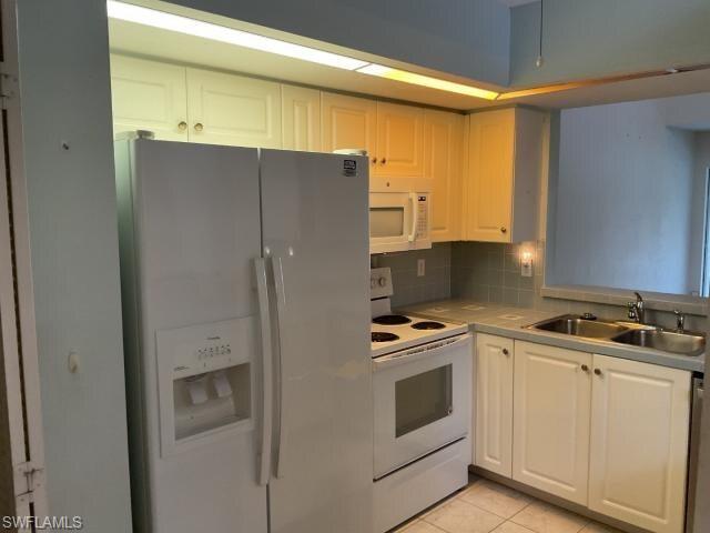 Kitchen with white appliances, tasteful backsplash, light tile patterned floors, light countertops, and white cabinetry