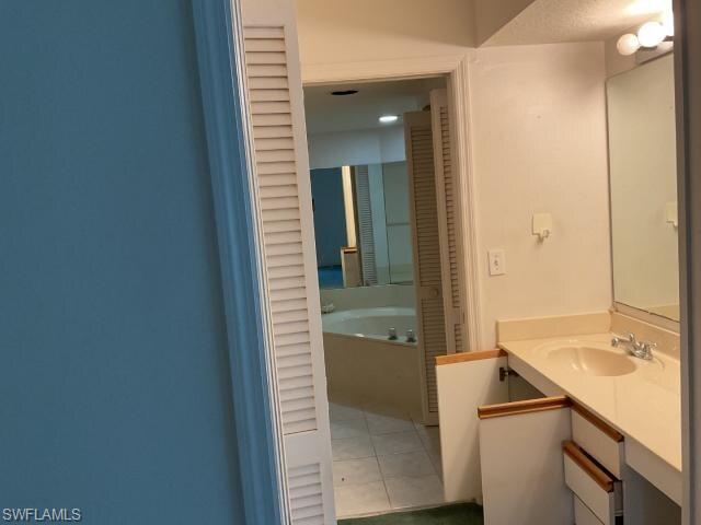 Full bath with vanity, a garden tub, light tile patterned floors, and a closet