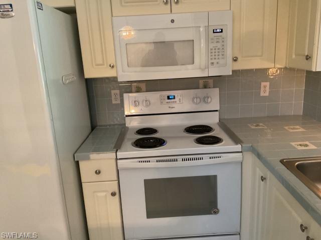 Kitchen with white appliances, tile counters, white cabinets, and backsplash