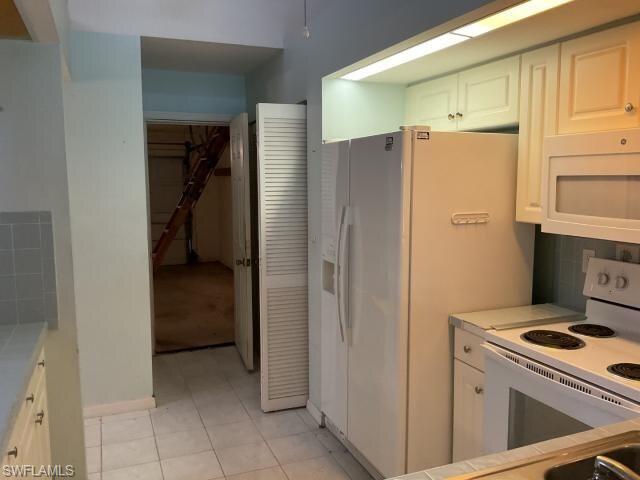 Kitchen featuring white cabinets, white appliances, light tile patterned floors, backsplash, and tile countertops