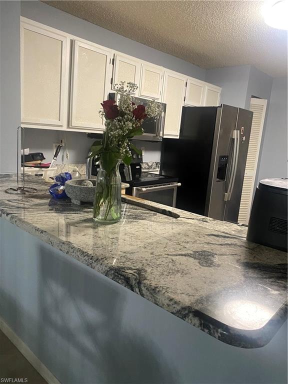Kitchen featuring dark stone countertops, a textured ceiling, white cabinetry, stainless steel microwave, and a peninsula
