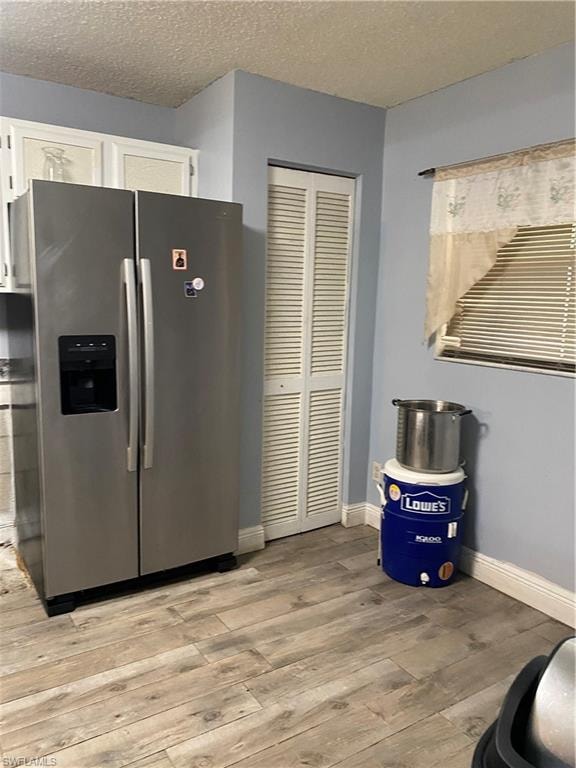 Kitchen with fridge, a textured ceiling, light wood-style floors, and white cabinets