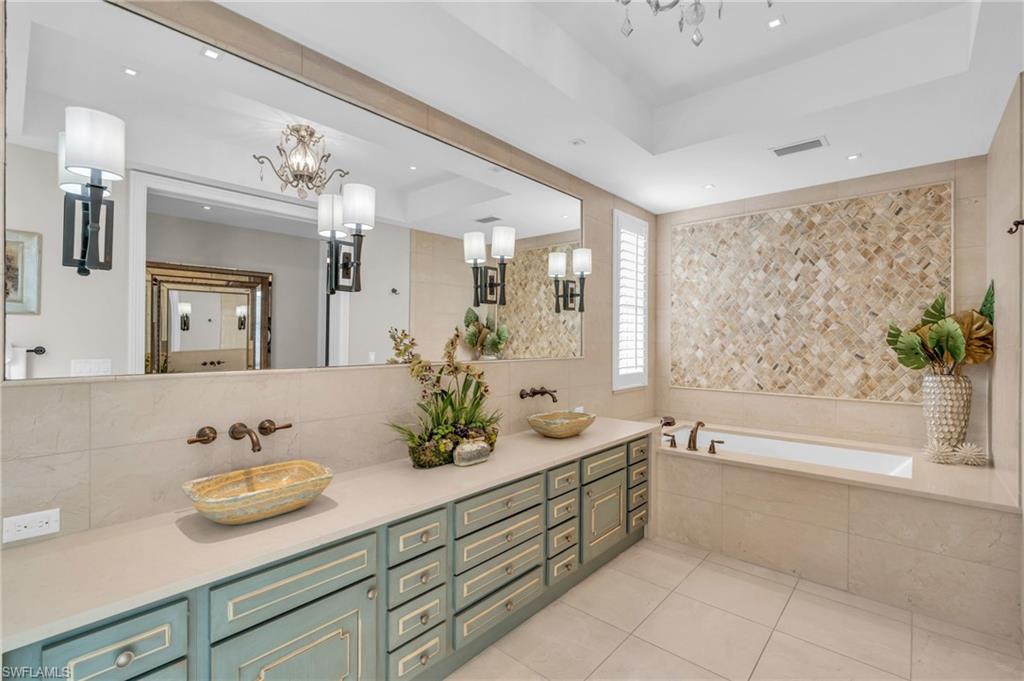 Bathroom featuring a raised ceiling, double vanity, a bath, light tile patterned floors, and a chandelier
