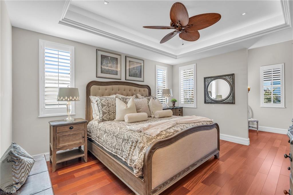 Bedroom with a tray ceiling, wood finished floors, and multiple windows