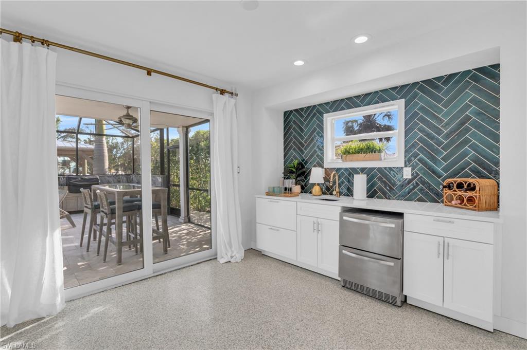 Bar with white cabinets, backsplash, light stone countertops, dark aggregate flooring, and a sunroom