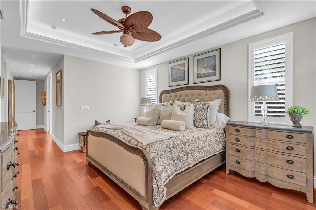 Bedroom with a tray ceiling, light wood finished floors, and a ceiling fan