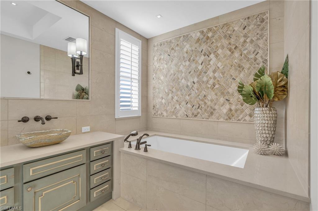 Full bath featuring tile walls, vanity, a bath, and light tile patterned flooring