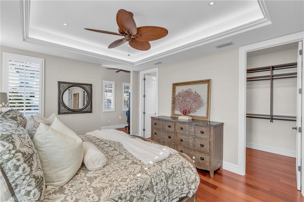 Bedroom featuring a raised ceiling, light wood finished floors, a spacious closet, and ceiling fan