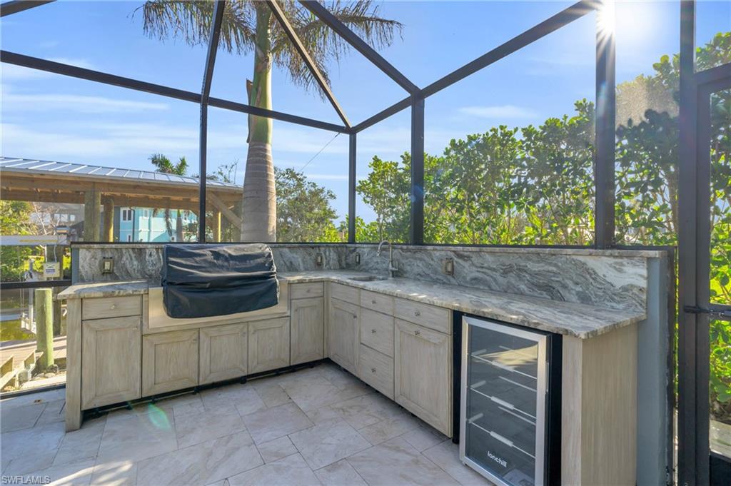 View of patio with beverage cooler, an outdoor kitchen, and glass enclosure