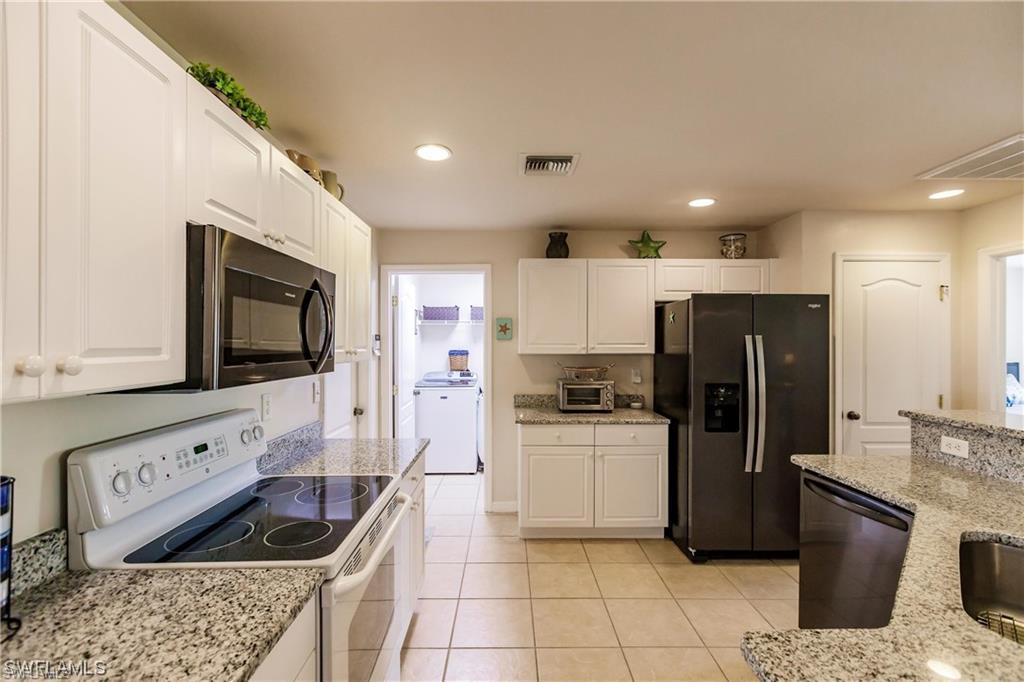 Kitchen with electric stove, fridge with ice dispenser, black microwave, white cabinets, and light stone countertops