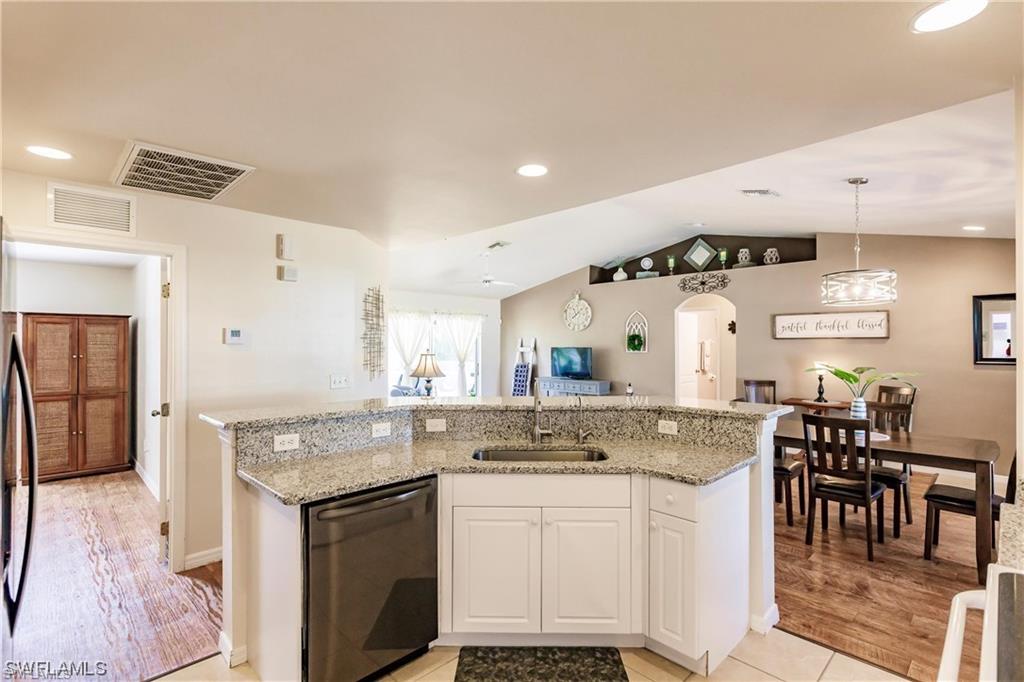 Kitchen with white cabinetry, appliances with stainless steel finishes, light stone counters, arched walkways, and a center island with sink