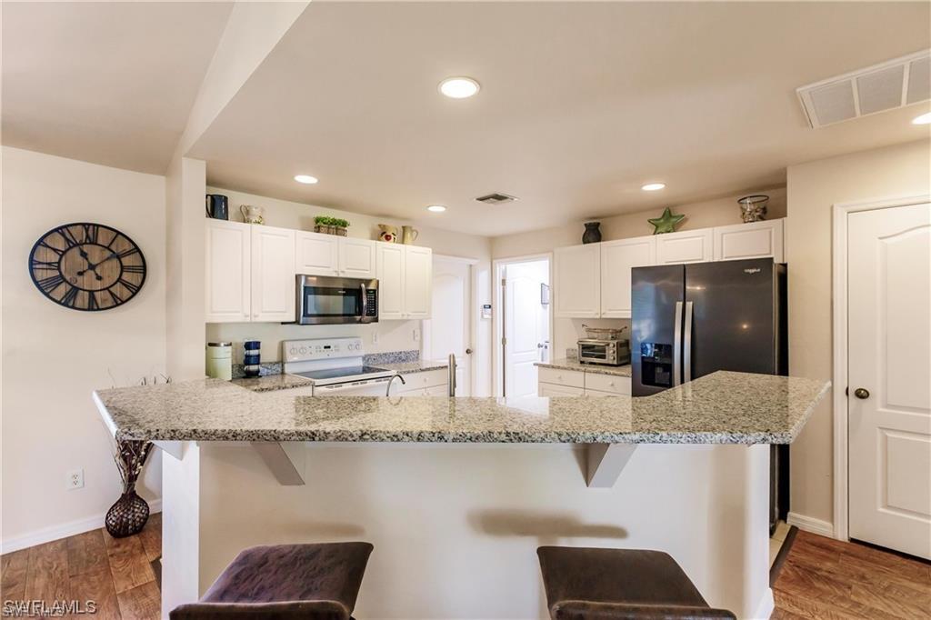Kitchen with dark wood-type flooring, white electric range, light stone counters, white cabinets, and recessed lighting