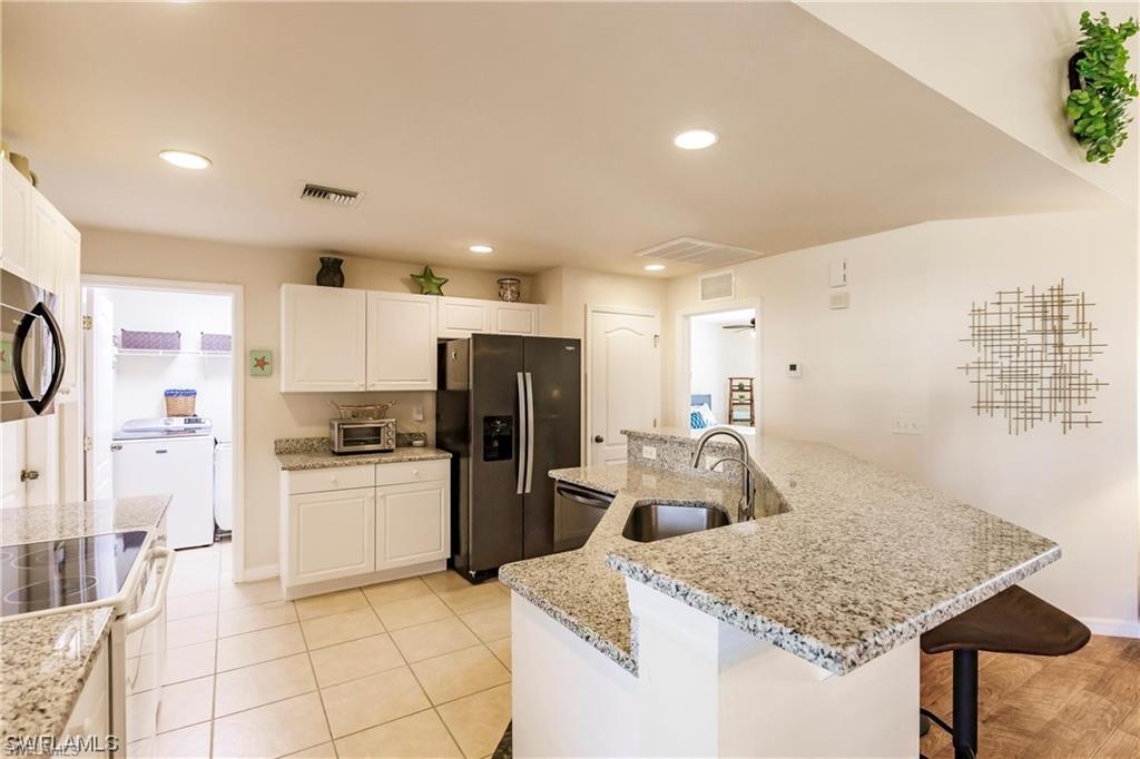Kitchen with an island with sink, appliances with stainless steel finishes, recessed lighting, white cabinets, and light stone counters